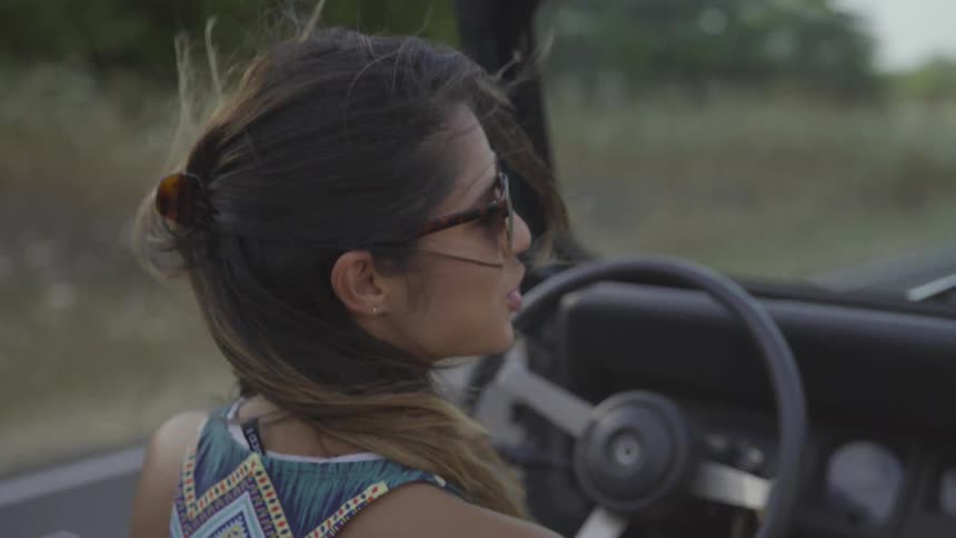 Woman driving a convertible with her hair blowing around her while talking to a passenger