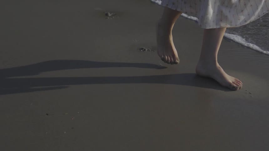 A barefoot person walks along the shore of a beach