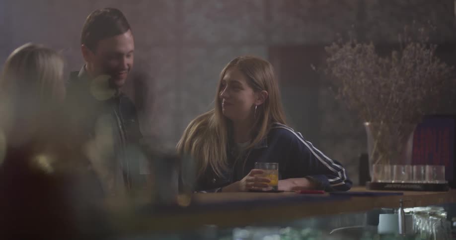 Two women sit at a bar and talk to a man who walked up to them