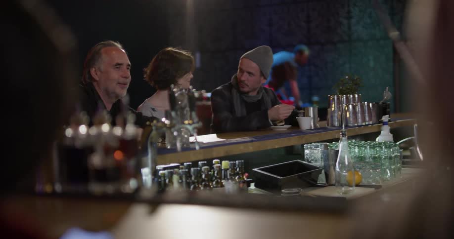 Two men and a woman sit at a bar talking