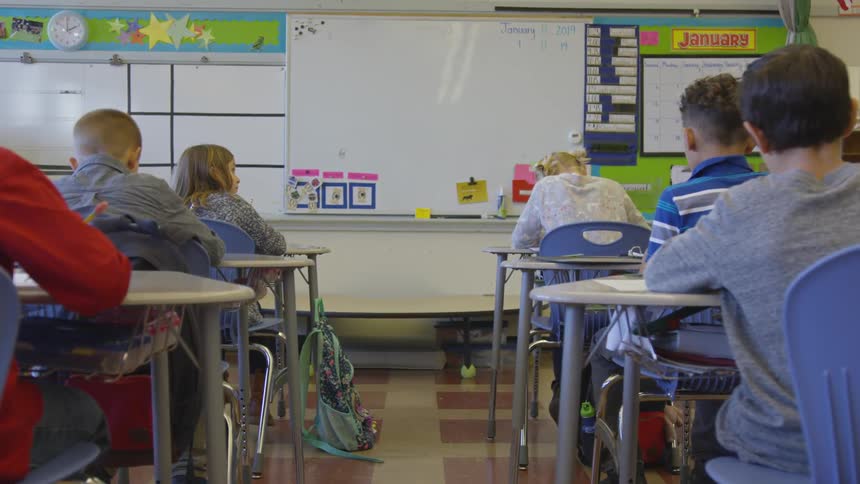 Classroom of students sit at desks writing