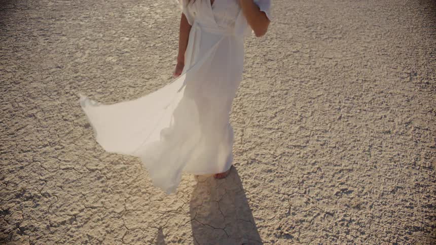 Woman in flowing white dress walks on sand