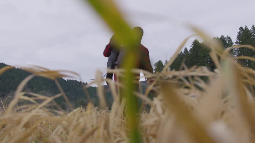 Man in ski mask carries smaller person over shoulder among tall grass during the day