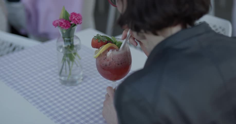 A woman is served a cocktail topped with a strawberry and a lemon and takes a sip