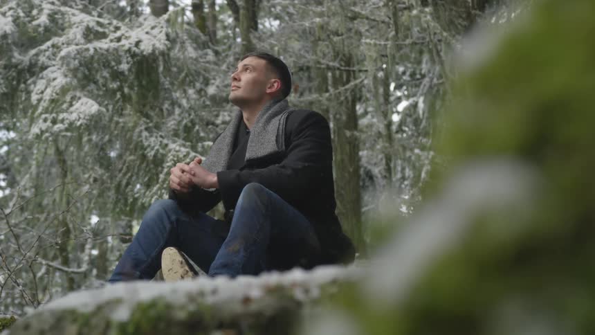 Man sits on the ground staring up at the falling snow