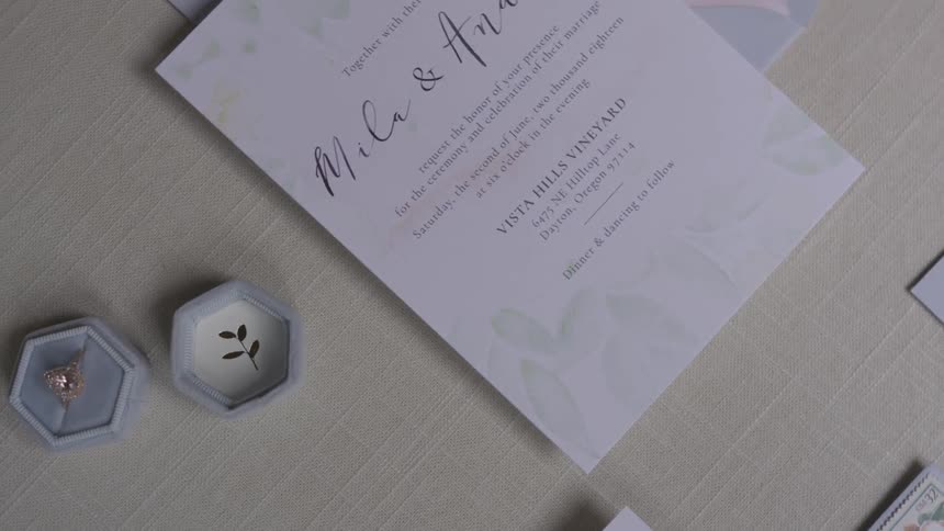 A ring sits on a table next to a wedding invitation