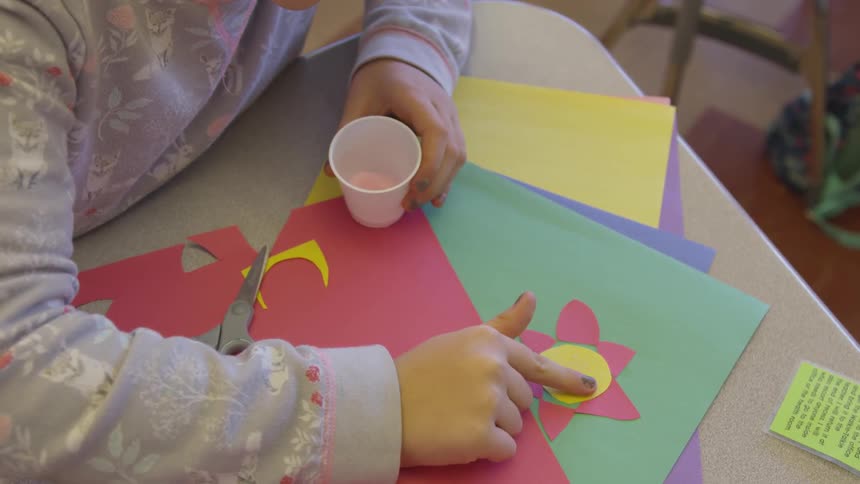 A young girl applies glitter to a craft made with construction paper