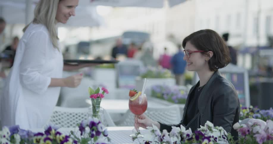 Seated woman gets served a drink at an outside restaurant