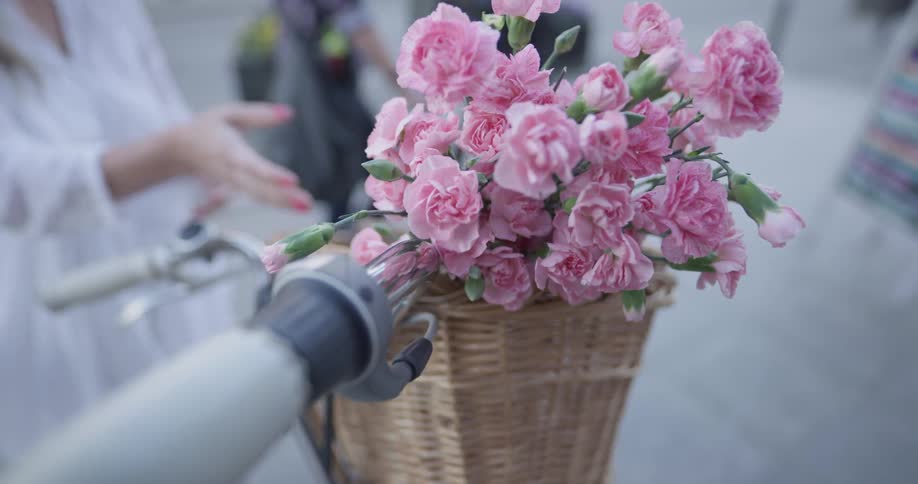 A woman takes flowers out of a basket that is on the front of a bike