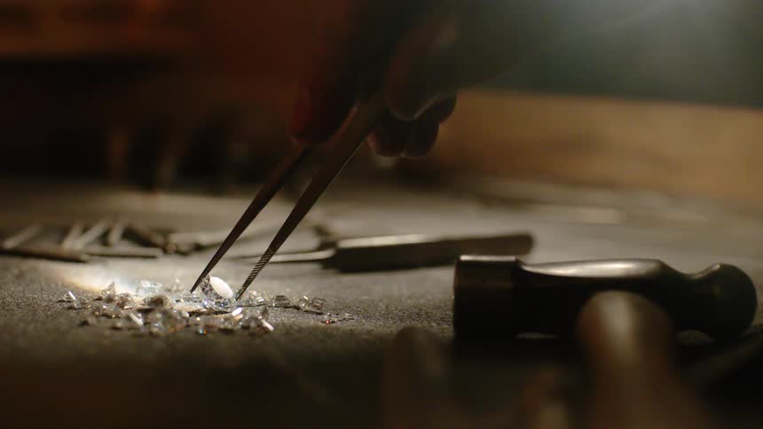 Tweezers pick up a single gemstone off the table