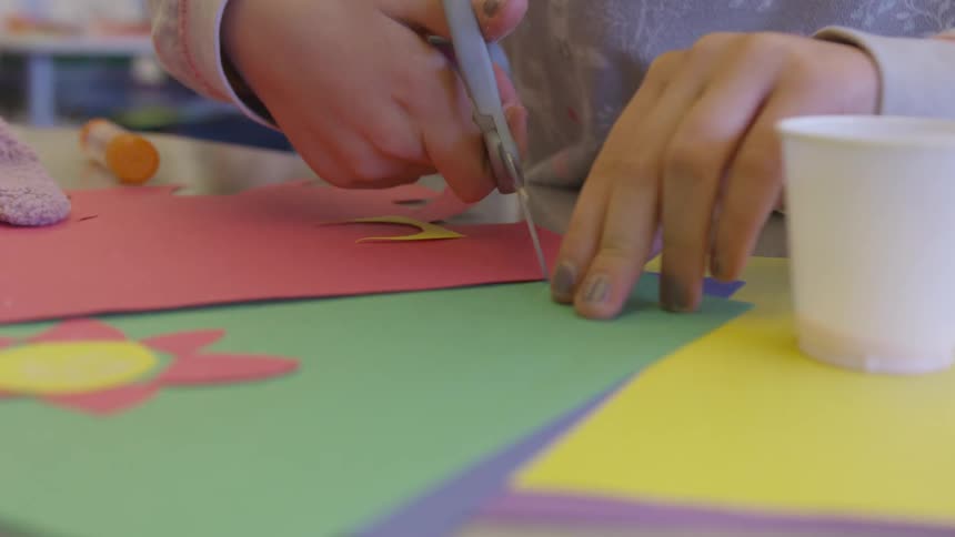 A young child is cutting pieces of colored card to create a picture