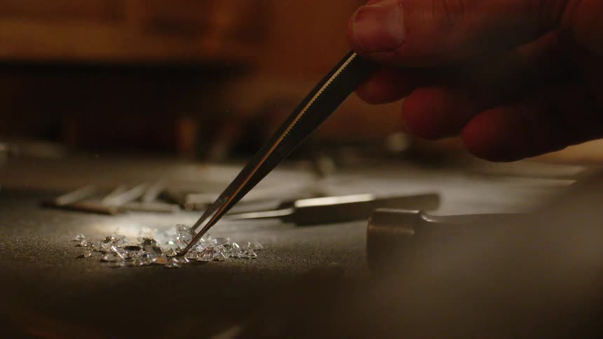 Careful hands picking up and grabbing a bright diamond with tongs on a felt mat in a workshop or jewelry store