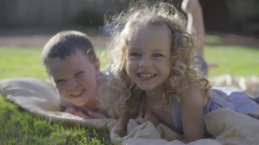 Two young children smile and kick their legs in the grass