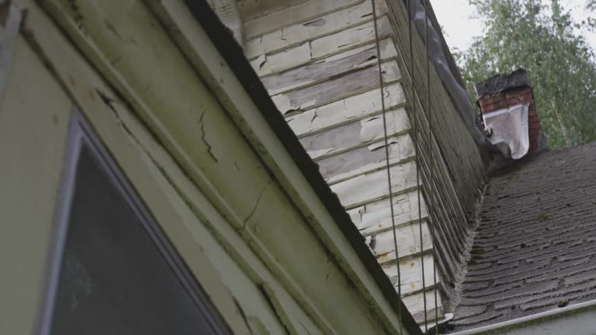 An old house has faded chipping paint and a beat up roof and chimney