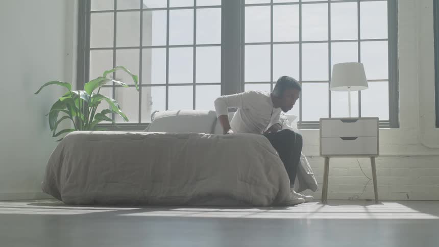 A black man puts on a set of headphones and leaves a bedroom
