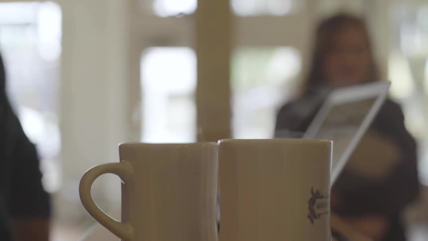 Two cups of steaming coffee with people working nearby