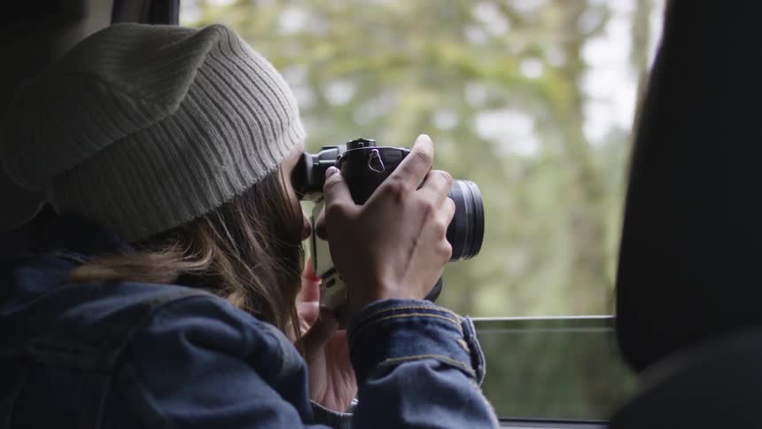 A woman points a camera out of a moving vehicle