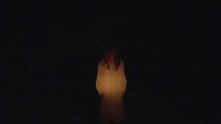 A woman wearing a white robe is standing in the dark with a light pointed to her