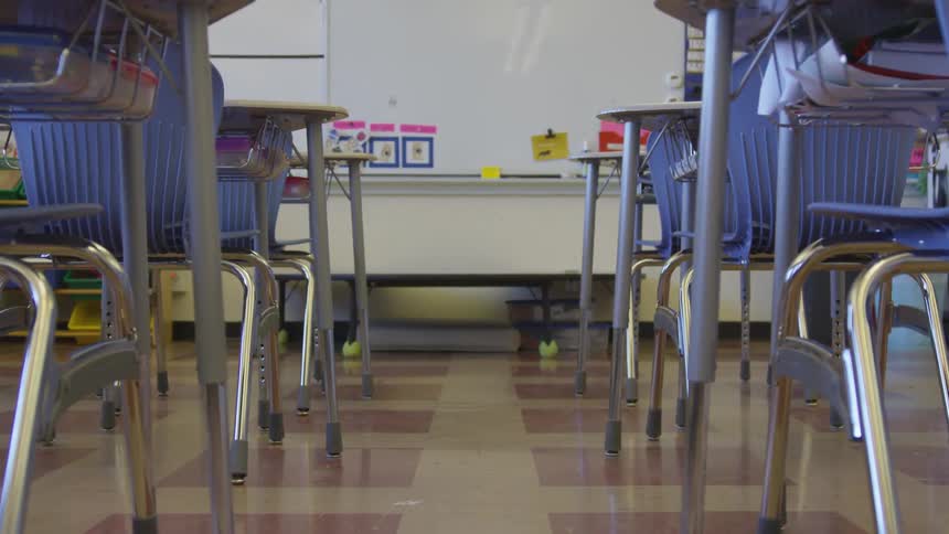 A classroom with desks and blue chairs with a whiteboard at the front of the room