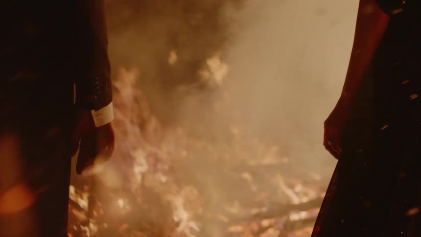A man and woman hold hands then let go overlooking a fire