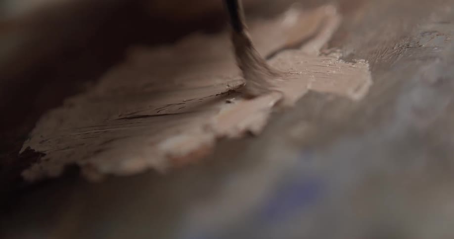 Someone paints with flesh tone paint on a canvas covered in dark paint