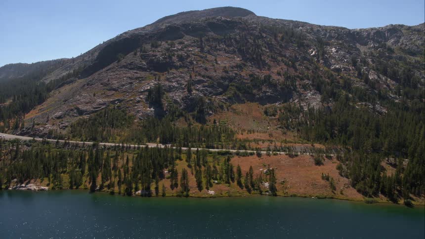 Car drives along road between mountain and water