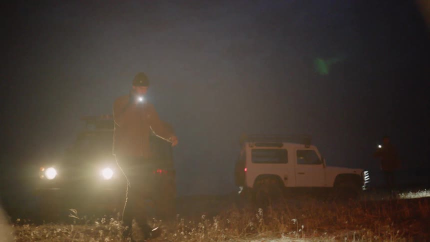 Two people shine flashlights in a field at night