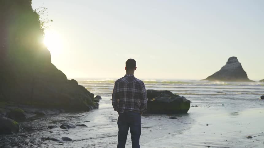 A man standing on the edge of the water during sunrise