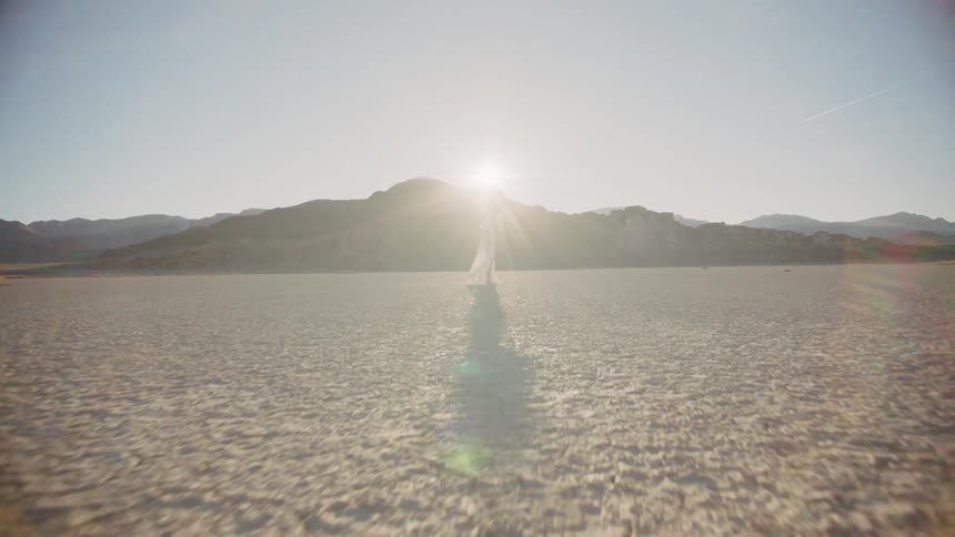A woman wearing a white dress walking on dry dirt in the sun