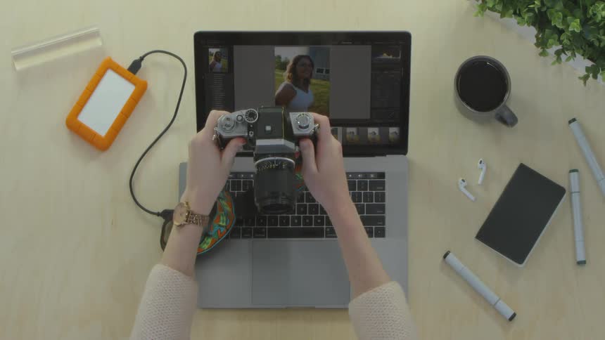 A woman's hands editing photos on a laptop and picking up a camera
