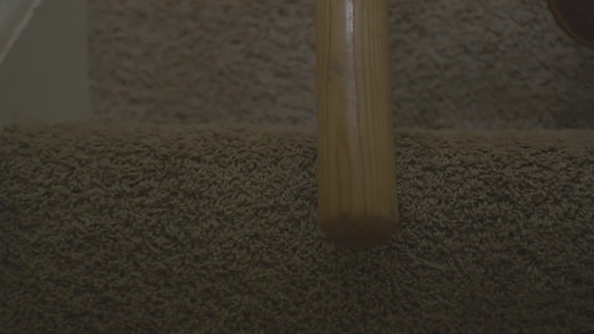 A baseball bat is being pulled up carpeted stairs