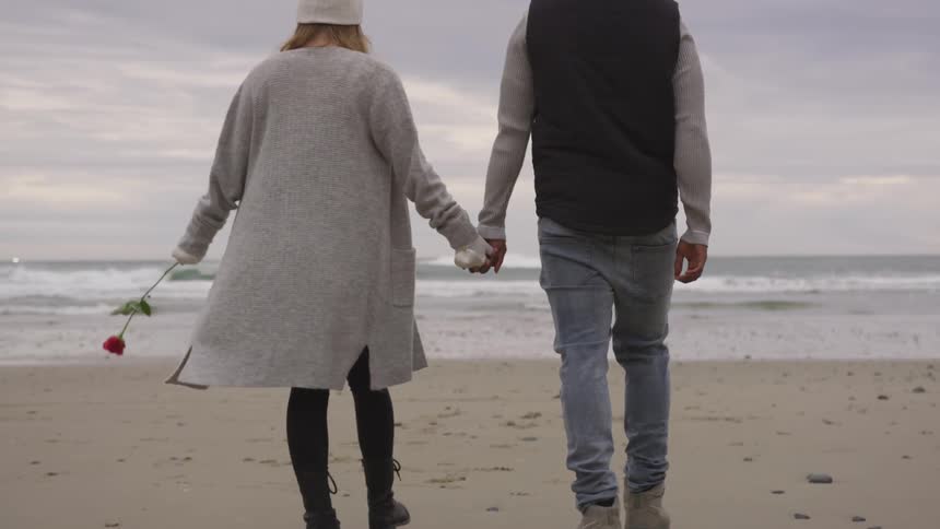 A man and woman holding hands, walk toward the ocean water