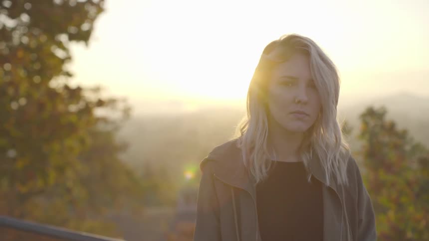 Woman looks down and up with the sun rising behind her