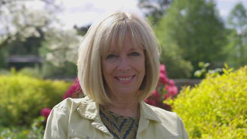 A woman smiling in a garden with flowers