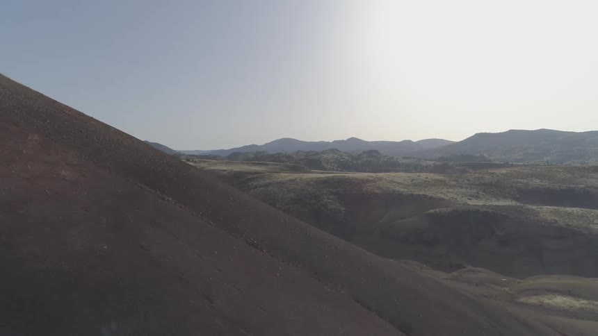 Flying through the valley of a mountain landscape of barren soil and dirt and rocks with some trees in the distance and sunny day