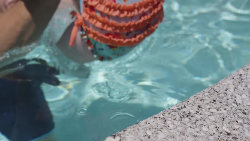 Toddler girl jumps into pool water into adults hands