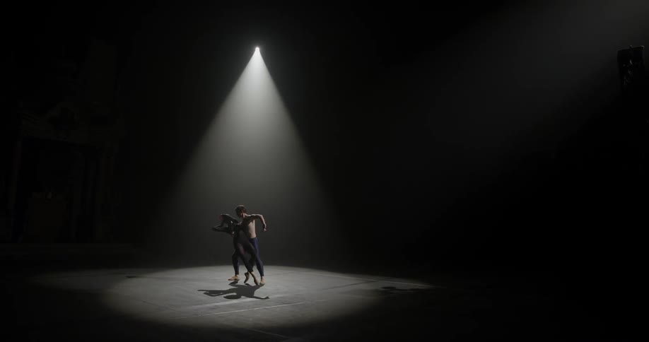A man and a woman performing a dance under a spotlight