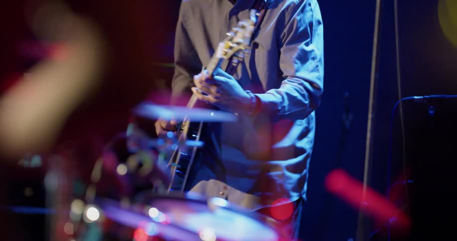 Man plays guitar as part of band on stage