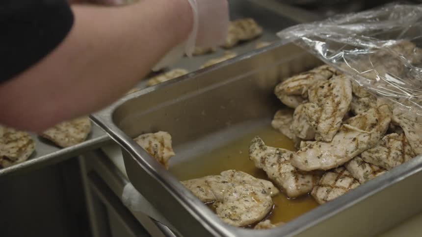 A culinary worker placing grilled chicken breasts on a baking tray