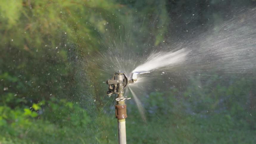 A water sprinkler is spraying water in a yard at day