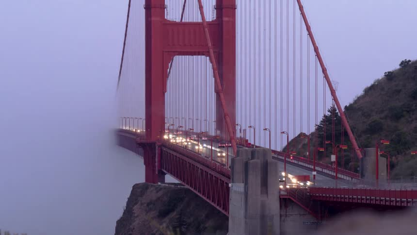 Cars drive over a suspension bridge through the fog