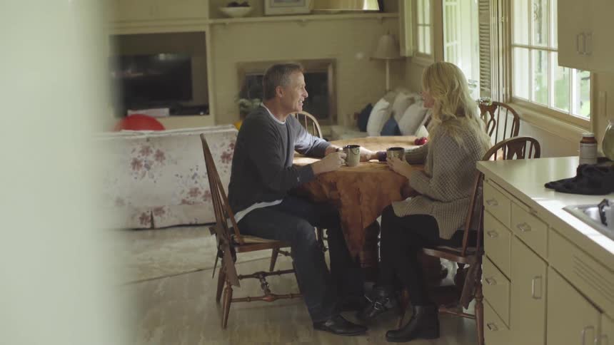 A man and woman drink coffee at a dining table at home