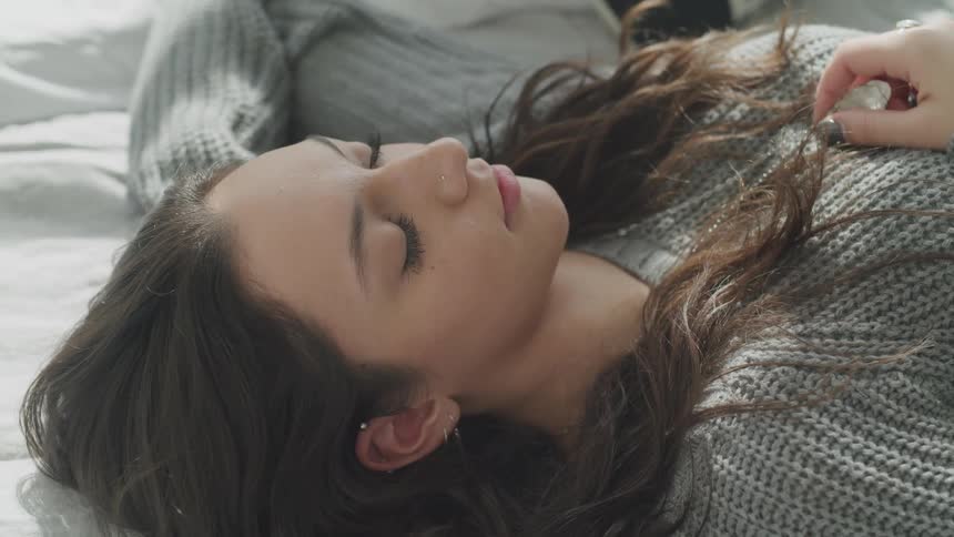 Woman in a sweater laying on her back in a bed
