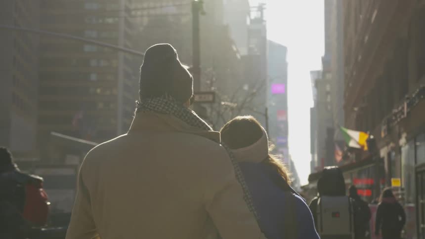 A man walks closely behind a woman on the sidewalk