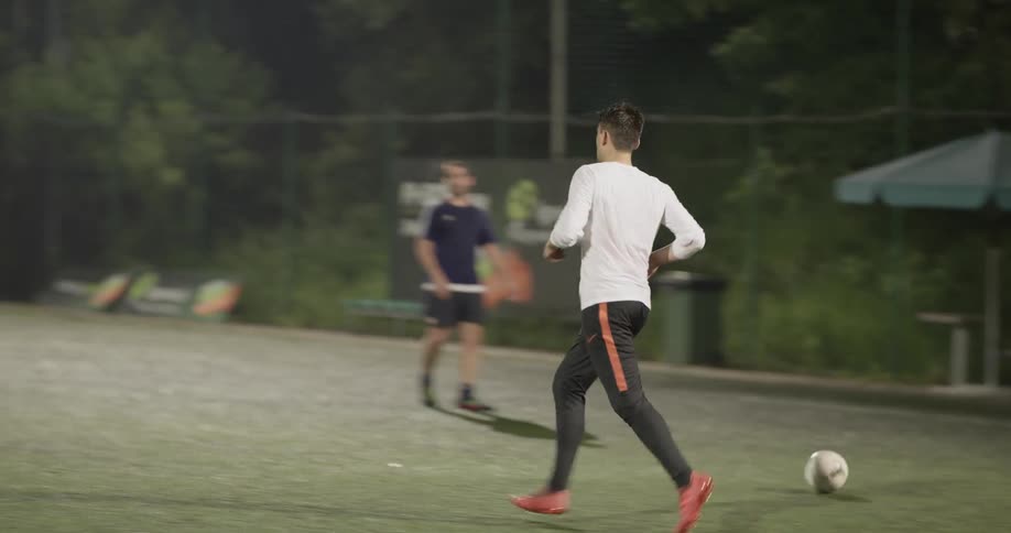A man dribbles a soccer ball back into play on a field at night