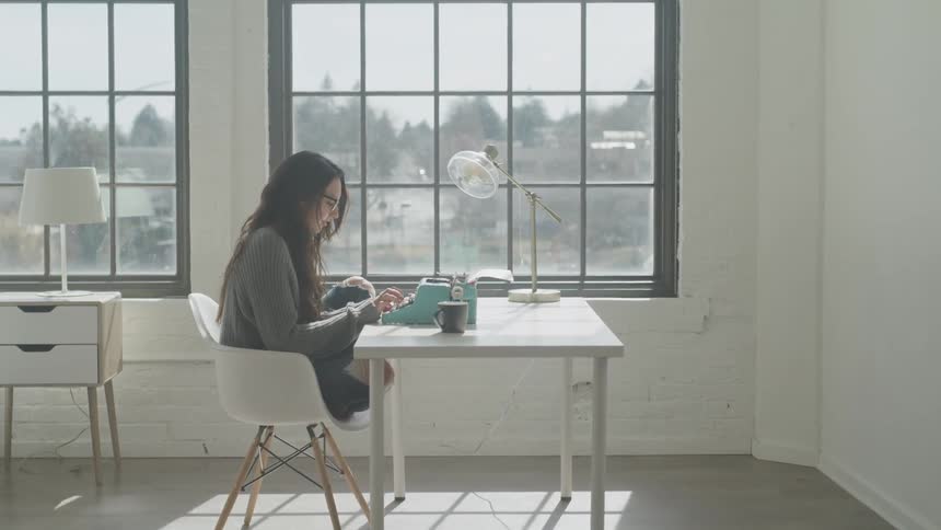 A woman types on a typewriter in front of a window
