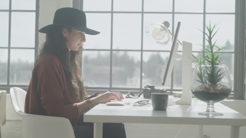 Woman wearing hat sits on the chair on a sunny day and types