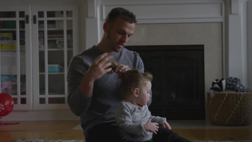 Man plats toddlers hair while sitting on floor
