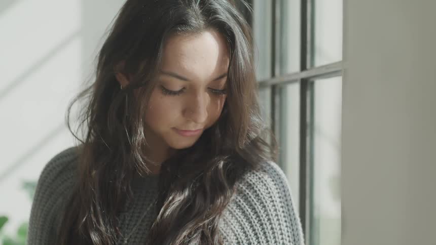 Woman looks down at her shoulder in front of a window in the daytime
