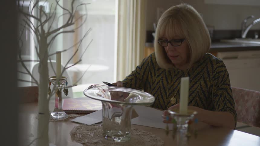 An elderly woman opening a letter at a table